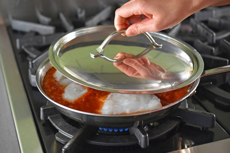 A lid is placed on the Poached Cod in Marinara Sauce in a stainless steel skillet.