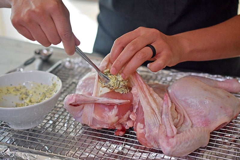 Tucking the softened herb butter underneath the skin of the spatchcocked chicken.