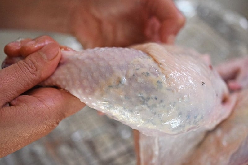 A closeup of a chicken leg with herb butter beneath the skin