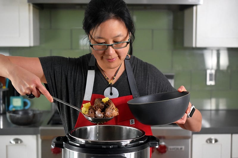 A woman is scooping Instant Pot Spicy Pineapple Pork out of an Instant Pot into a bowl.