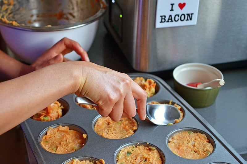 Someone flattening the spicy tuna cake mixture into a muffin pan with the back of a spoon.