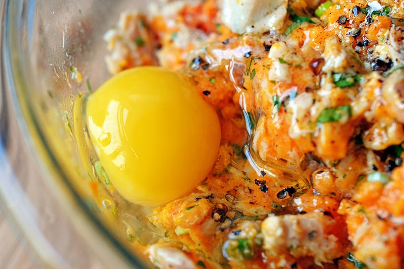 A raw egg is added to the spicy tuna cake mixture in a bowl.