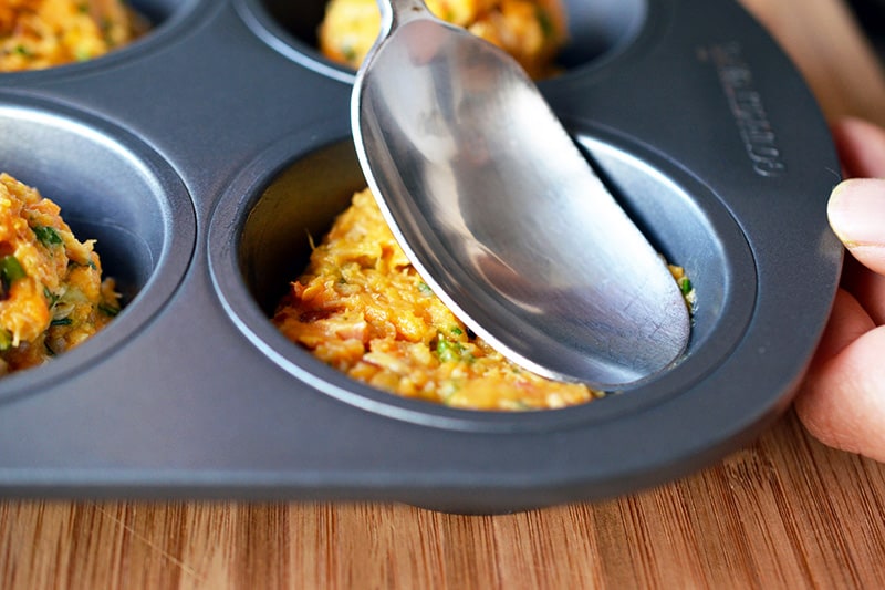 Flattening the spicy tuna cakes into the muffin tin with the back of a spoon.