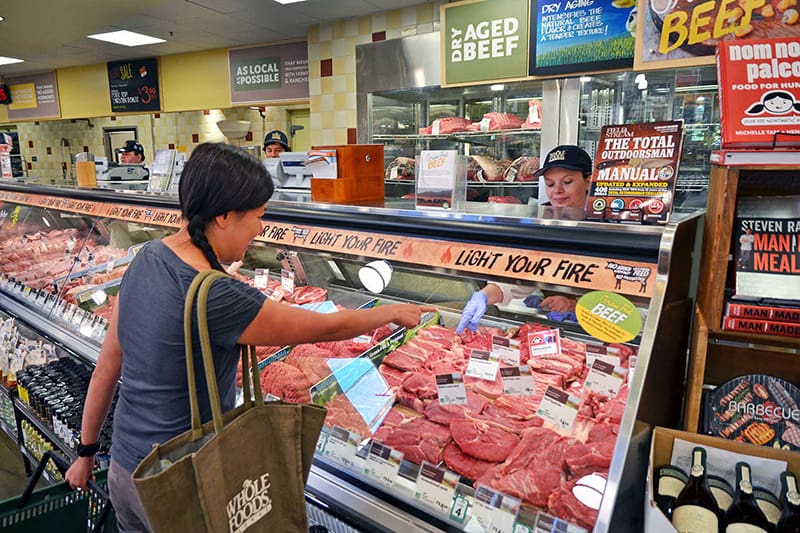 A picture of an Asian woman shopping for meat at the butcher counter at Whole Foods Market.