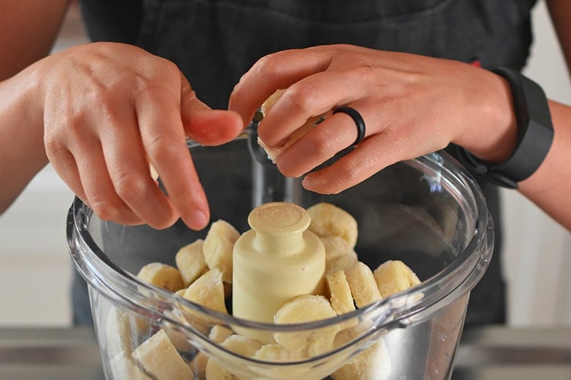 Someone putting frozen banana chunks into a food processor.