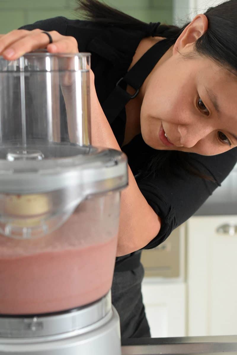 A woman watches the ingredients in the food processor as it's being mixed.