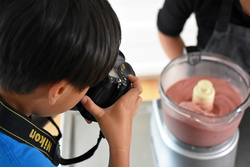 A young boy takes a picture of the strawberry banana ice cream in the food processor.