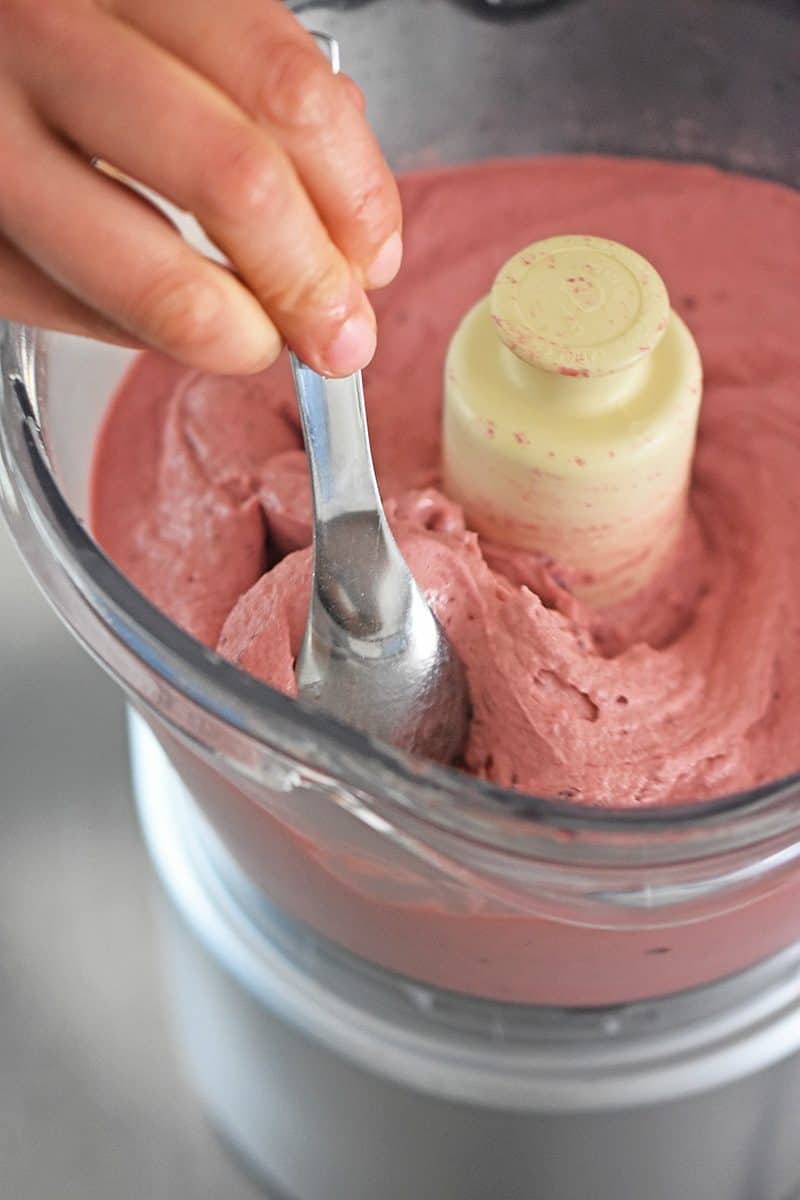 Someone putting a spoon in the strawberry banana ice cream mixed in a food processor