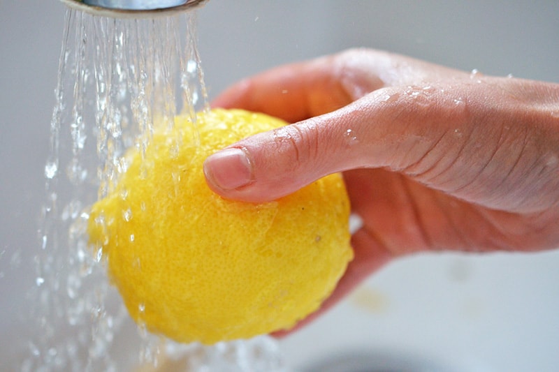 A shot of someone washing a lemon under a kitchen faucet.
