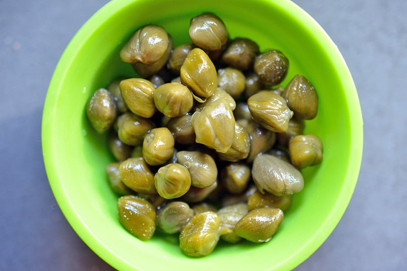 An overhead shot of drained capers in a green silicone prep bowl.