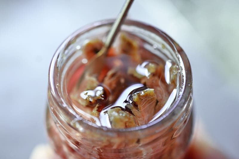 A closeup of an open jar of anchovies in olive oil with a spoon inside. 