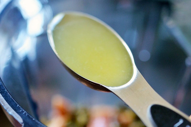 A shot of a spoonful of lemon juice positioned over an open blender container filled with Tonnato Sauce ingredients.