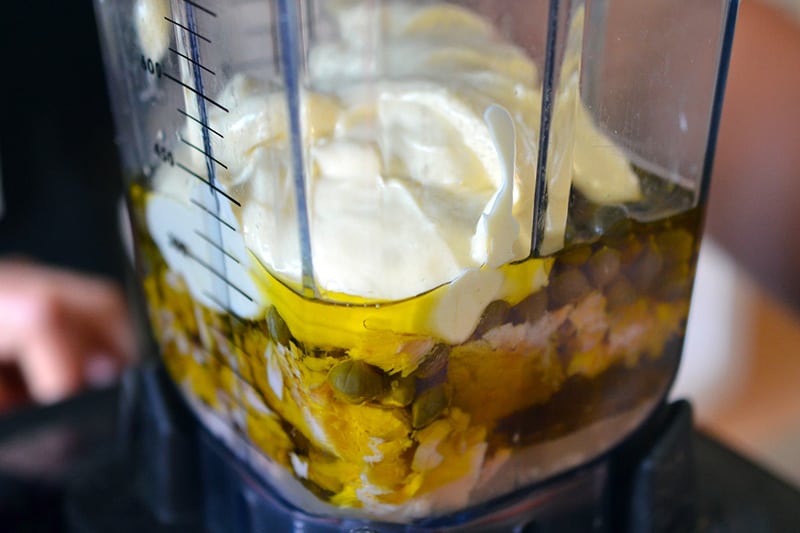 A side shot of a blender filled with all of the Tonnato Sauce ingredients before it is turned on.