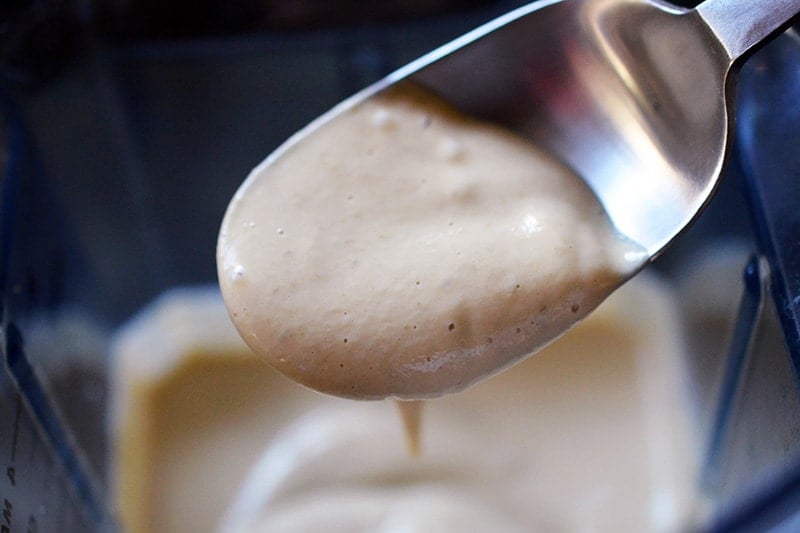 A spoon filled with a thick, beige colored sauce from a blender, keto Tonnato Sauce 