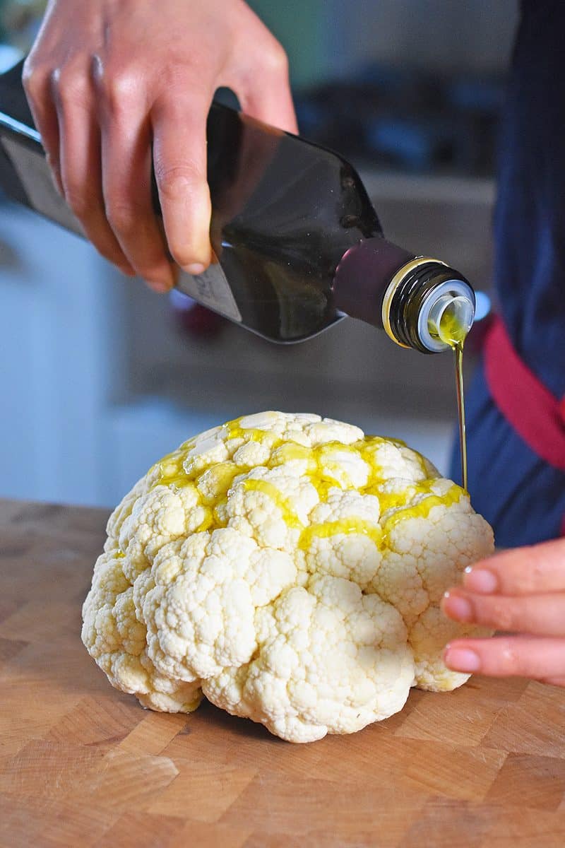 Pouring olive oil on top of a small cauliflower head.
