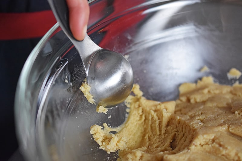 A close up of someone scooping the cookie dough with a measuring spoon.