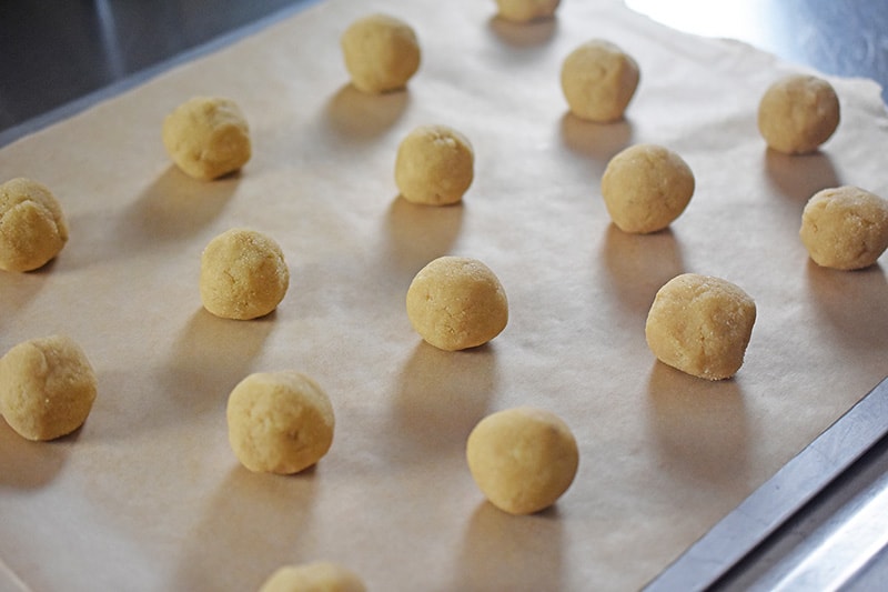 Unbaked cookie dough balls are on a parchment lined cookie sheet.