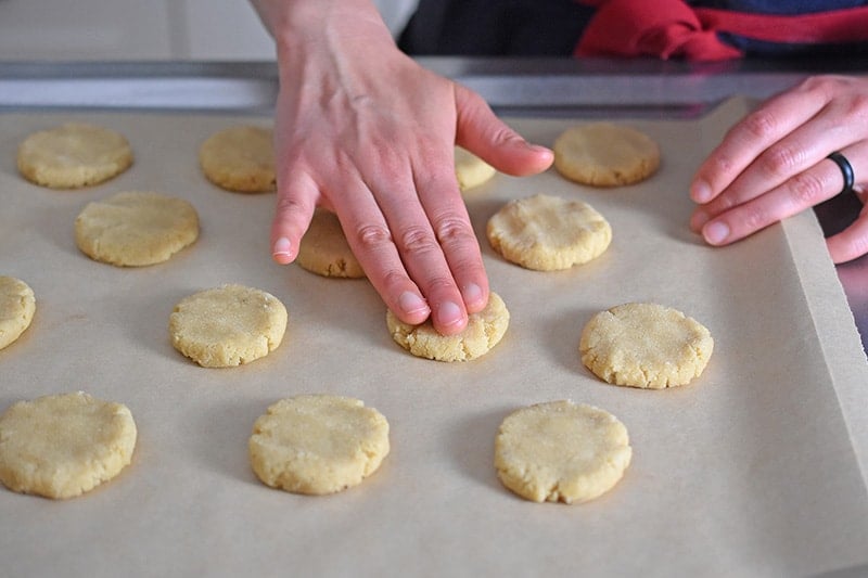 A hand is smushing the raw cookie dough into flat cookies.