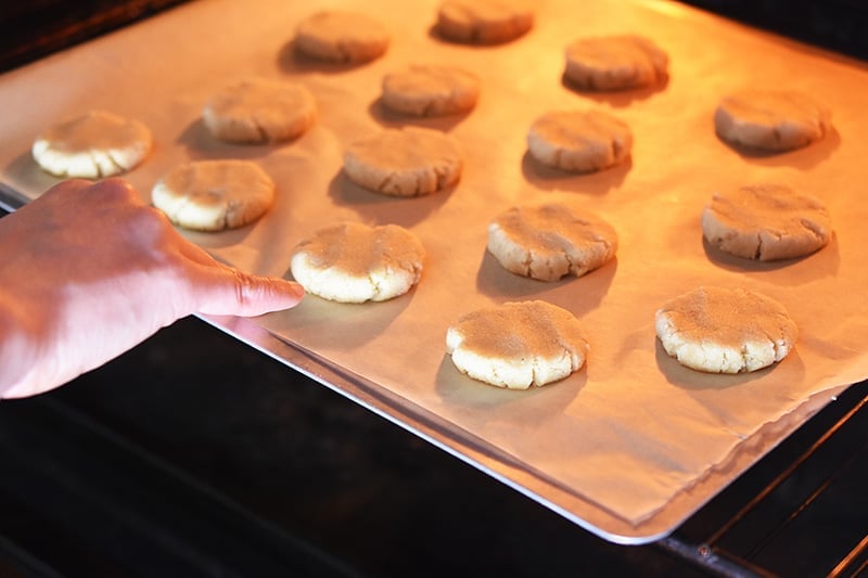 A hand is pushing a cookie sheet filled with cookies into the oven.