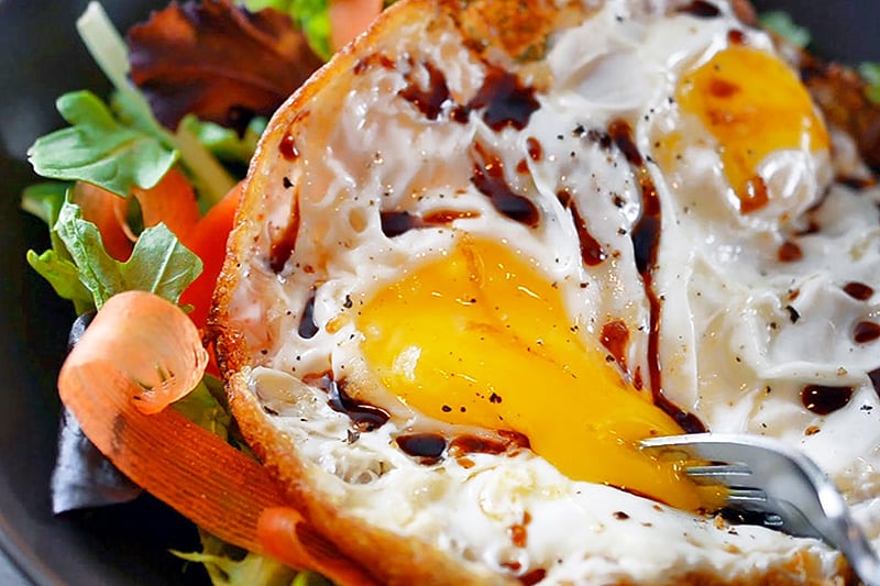 A fork is popping the runny yolk in a Sunnyside Salad 