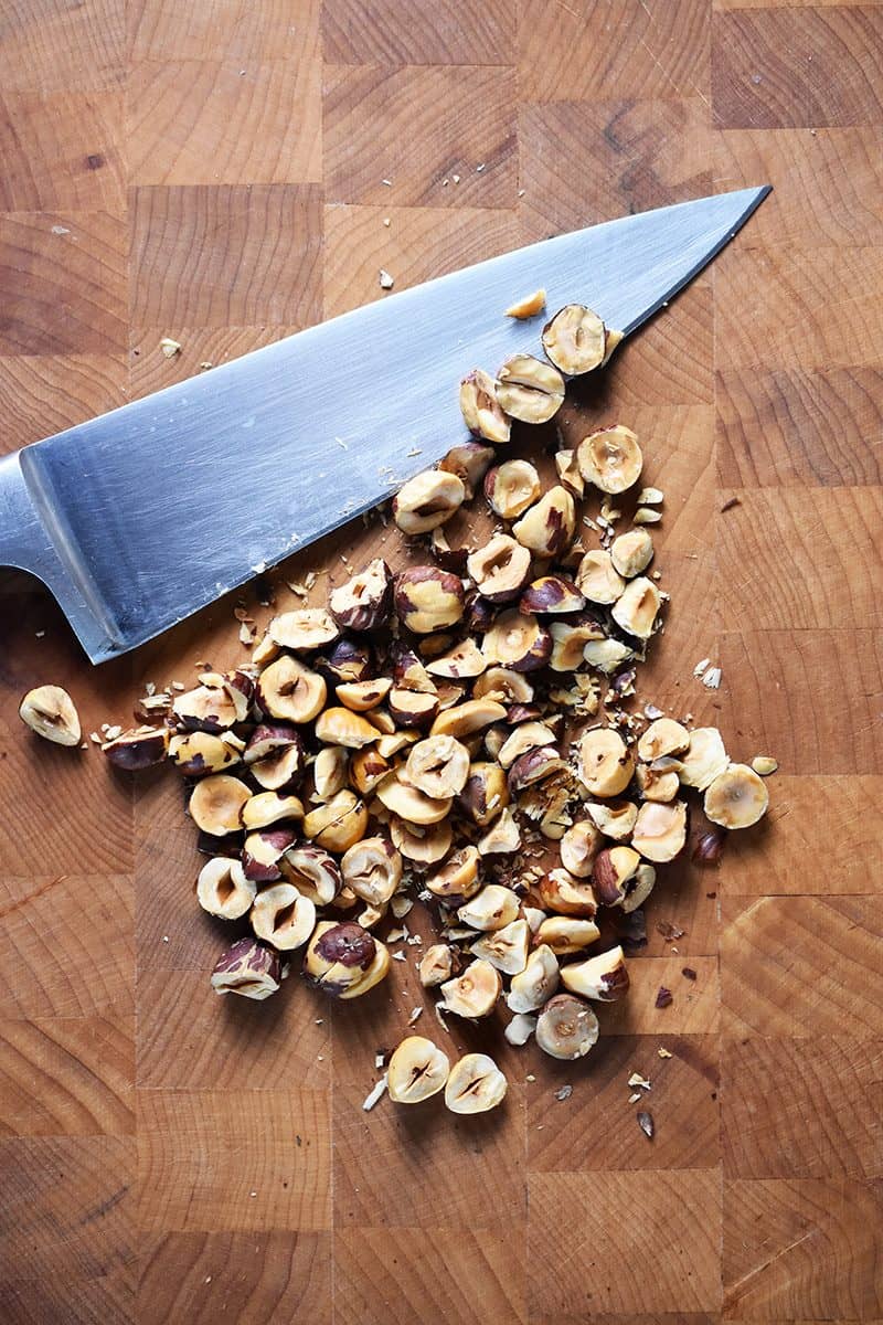 Chopped hazelnuts on a cutting board with a chef's knife.