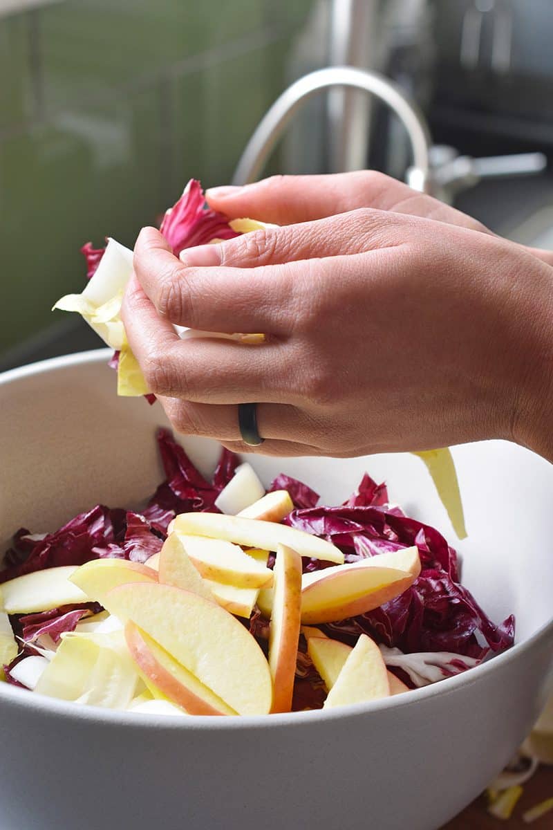 Combining the endives and apples in a bowl.