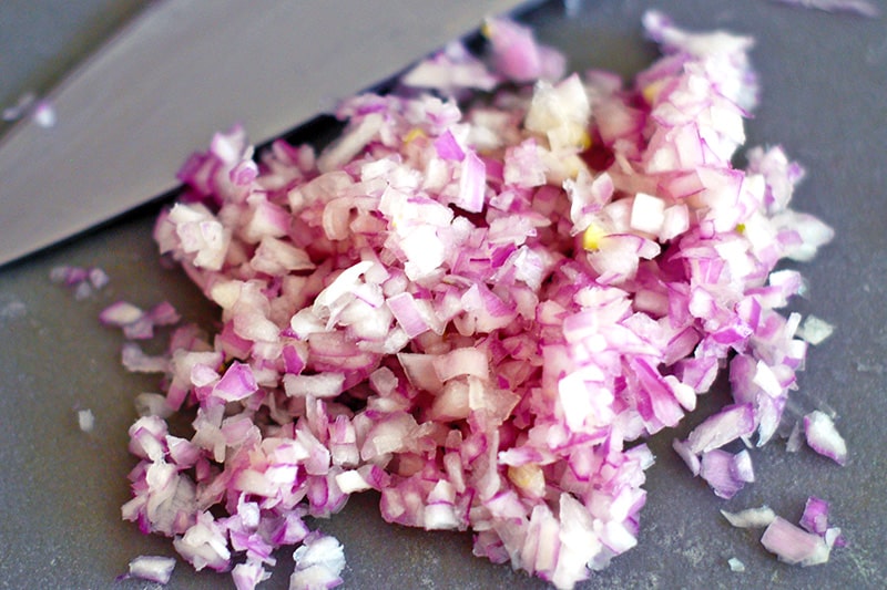 A close-up of finely minced shallots on a cutting board.
