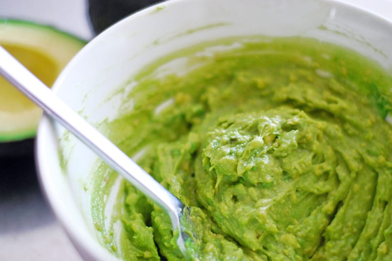 A white bowl containing guacamole that has been mashed with a fork.