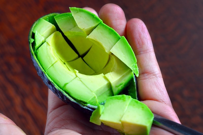 Half an avocado is diced into cubes and is held in someone's hand.