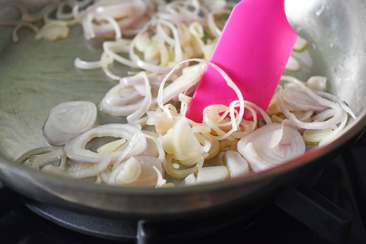Stirring sliced shallots in a frying pan with a silicone spatula