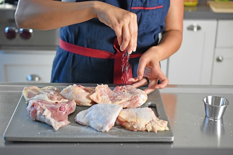 Sprinkling salt on chicken thighs on a cutting board 