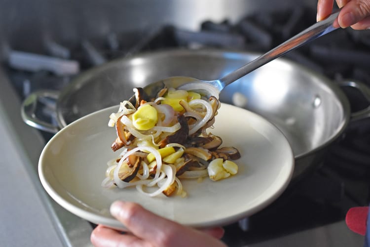 Transferring the sautéed aromatics and mushrooms from the pan to a plate.