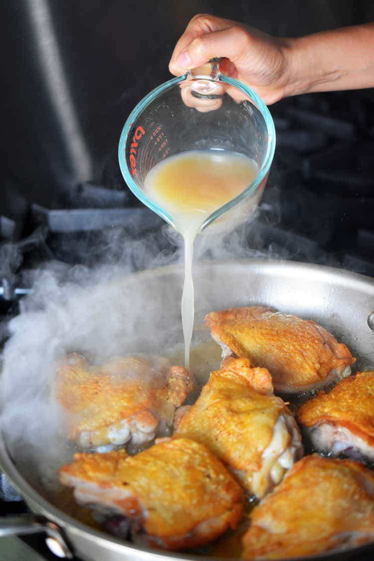 Pouring bone broth into a pan of Cantonese Crispy Chicken Thighs 