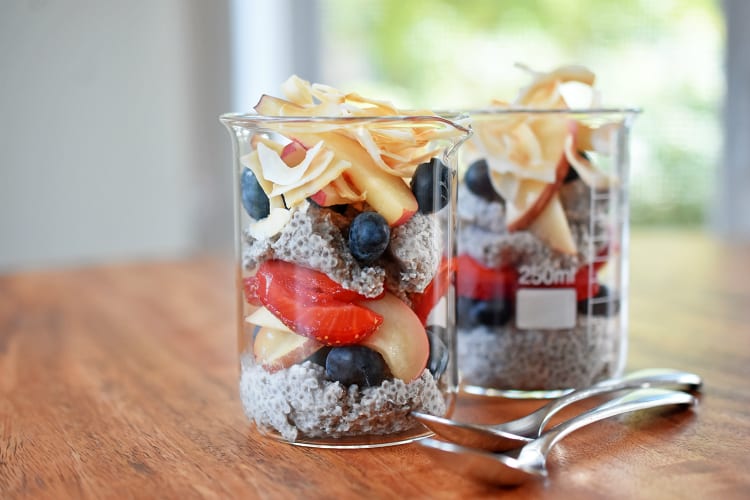 Two jars of coconut chia pudding layered with fresh fruit and toasted coconut,