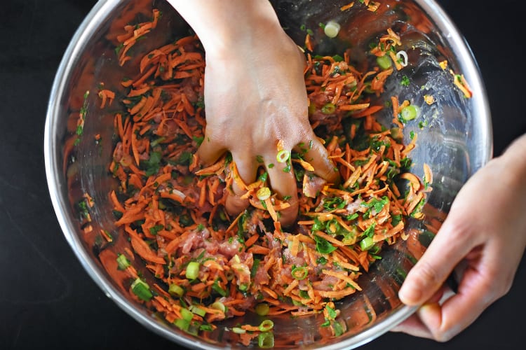 Using hands to mix the raw ingredients of Curry Turkey Bites in a large silver bowl.