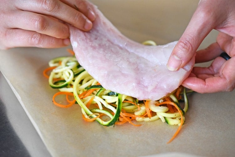 Placing a piece of fish on top of the spiralized vegetables on a piece of parchment paper. 