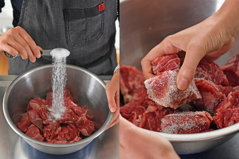 Salting the beef cubes in a silver bowl.