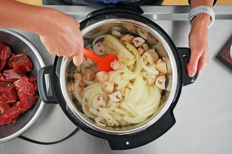 An overhead shot of someone mixing mushrooms and onions in an Instant Pot