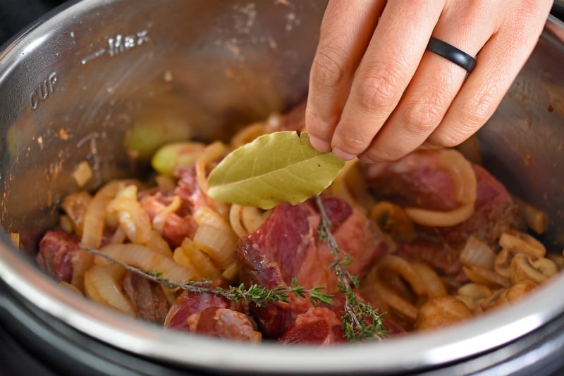 Adding a dried bay leaf and thyme sprigs to Instant Pot Beef Stew 