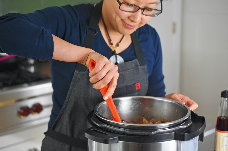 A smiling woman stirring Instant Pot Beef Stew in an open Instant Pot.