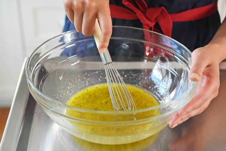 A person is whisking the Lemon Garlic marinade in a glass bowl for Whole30, paleo, and keto chicken foil packets.