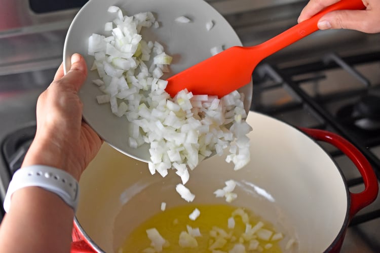 Adding diced onions to a stockpot to make Pork and Napa Cabbage Soup 