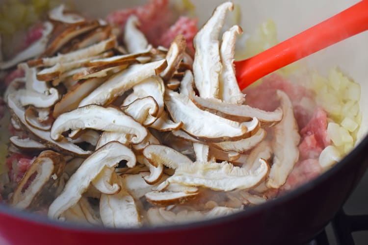 Sliced shiitake mushrooms are added to the pot with the ground pork and diced onions