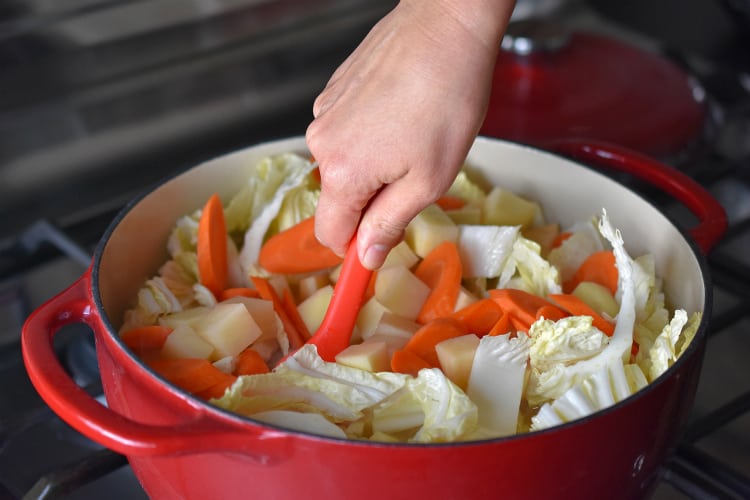 Stirring in sliced Napa cabbage and carrots into the pot.
