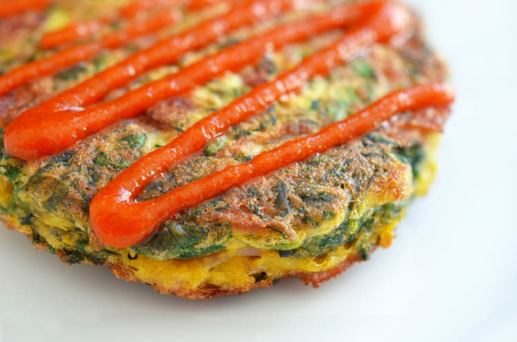 A closeup of gluten-free and paleo Egg Foo Young with a squiggle of Whole30 sriracha on top.