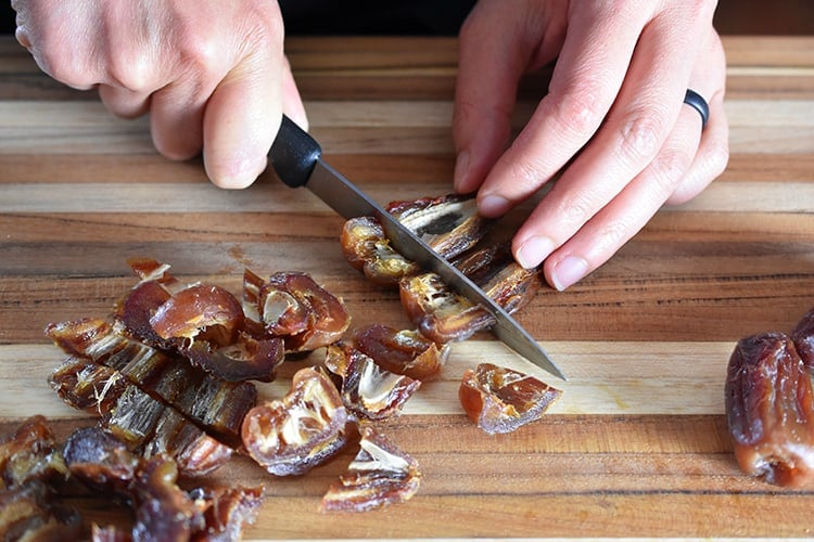 Someone chopping up pitted Medjool dates on a cutting board.