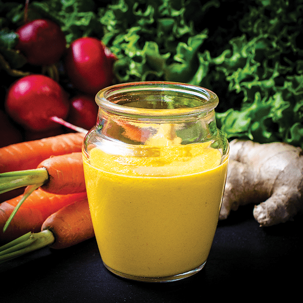 A jar of yellow sauce with vegetables in the background.