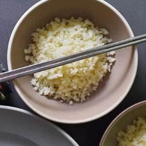 An overhead shot of cauliflower rice in a bowl topped with silver chopsticks