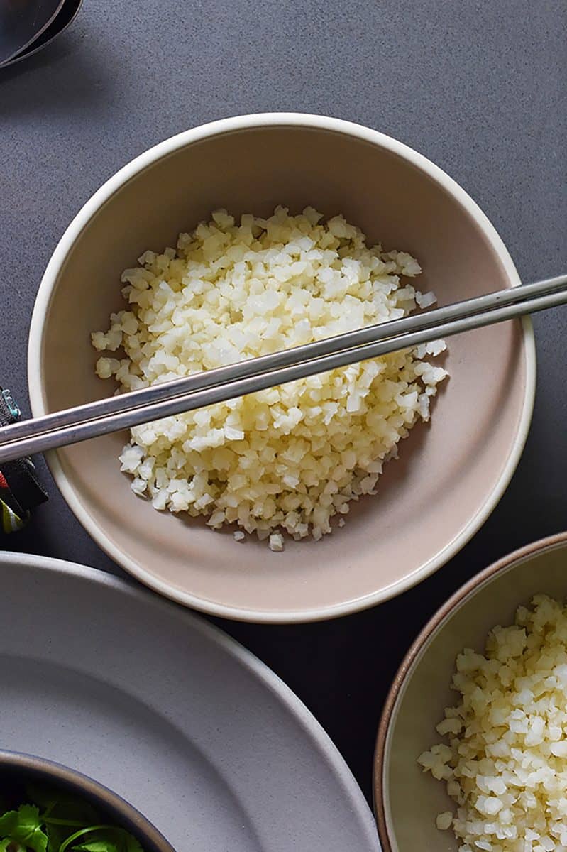 An overhead shot of Simple Cauliflower Rice in a bowl topped with silver chopsticks