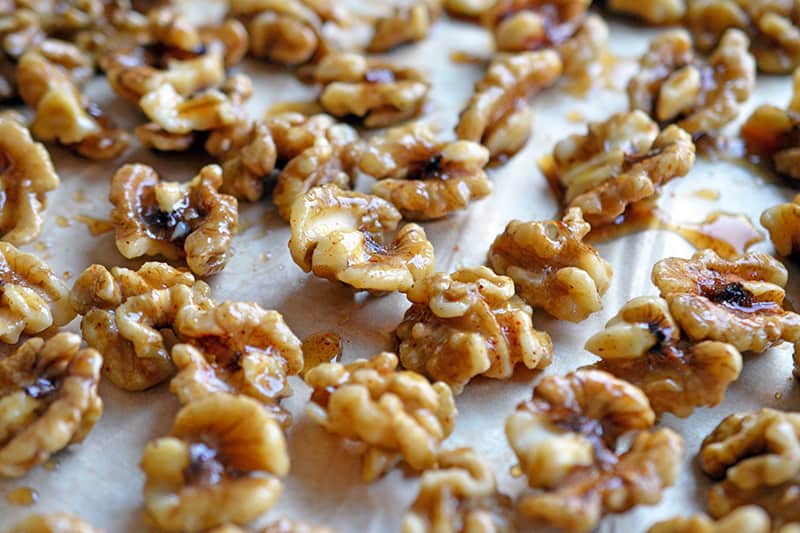 Maple spiced walnuts spread out on a piece of parchment paper.